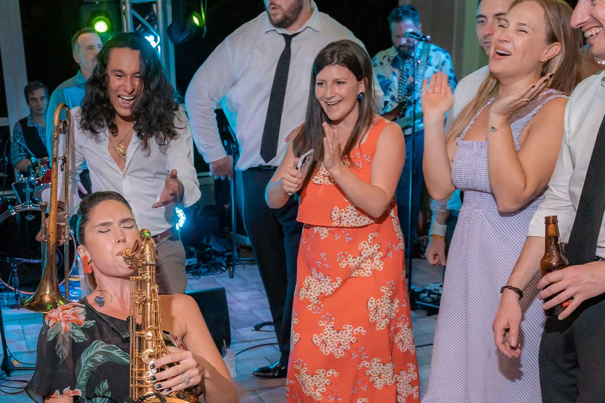 Amy Cyr performing saxophone surrounded by smiling guests at a reception